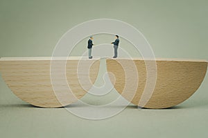 Miniature businessman stand on wood seesaw on endwise and shaking hands. Business, management