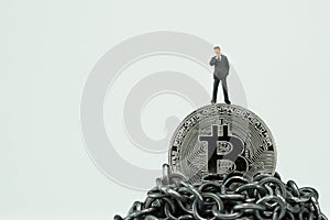 Miniature businessman standing on Bitcoin on top of chain mountain thinking about high future value