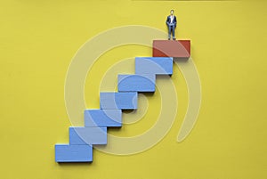 A miniature businessman at the top of stairway. Concept of success business or career