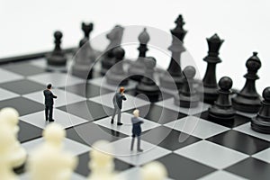 Miniature businessmen standing on a chessboard with a chess piece on the back. as background business concept with copy space.