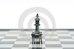 Miniature businessmen standing on a chessboard with a chess piece on the back. as background business concept with copy space
