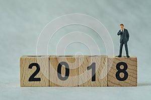 miniature businessmen thinking and standing on wooden block 2018 with white background as happy business new year concept