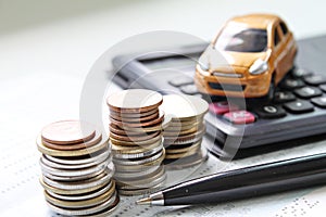 Miniature car model, coins stack, calculator and saving account book or financial statement on office desk table