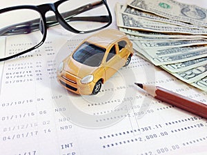 Miniature car model, pencil, eyeglasses, money and savings account passbook or financial statement on white background