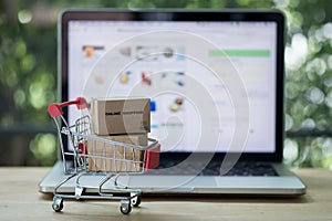 Miniature cardboard boxes in shopping cart with laptop computer