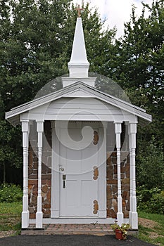 Miniature chapel reproduction in front of row of trees