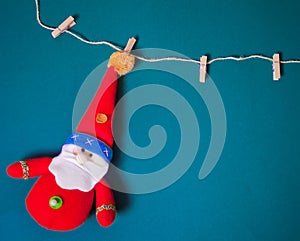 Miniature Christmas funny toy Santa hanging on the clothes pin on a blue background, Classic blue trend color 2020 year