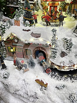 miniature Christmas scene of two people in a train station waiting on the platform, a train coming out of the tunnel and people