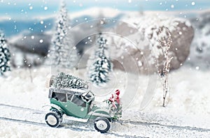 Miniature classic car carrying a christmas tree on snowy road in winter