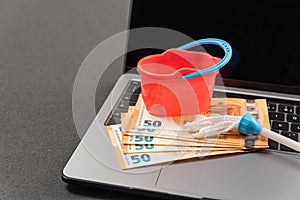 Miniature cleaning tools and cash euros on laptop keyboard. Online cleaning services. Concept of money laundering via the Internet