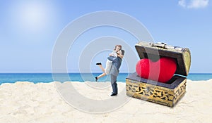 Miniature couple with red heart in treasure box on tropical beach, love and romance concept