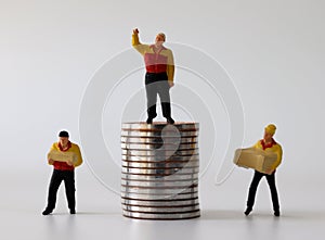 Miniature courier standing on pile of coins and miniature couriers standing next to pile of coins.
