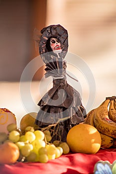 the miniature doll sits next to some fruits and a bunch of grapes