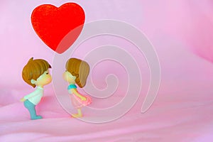 The Miniature dolls of couple boy and girl kiss and have big red heart on above with pink background for Valentine`s Concept