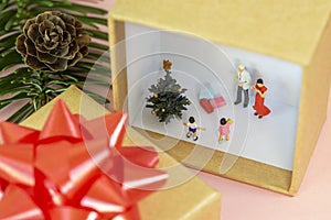 A miniature family is celebrating christmas in a gift box with a little christmas tree