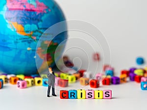 Miniature figure businessman in dark blue suit standing backside of colorful of CRISIS alphabet and globe in the background and th
