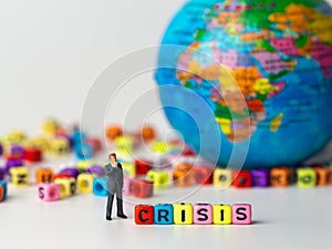 Miniature figure businessman in dark blue suit standing backside of colorful of CRISIS alphabet and globe in the background and th photo