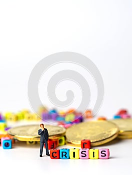 Miniature figure businessman in dark blue suit standing backside of colorful of CRISIS alphabet and golden coin and thinking of th