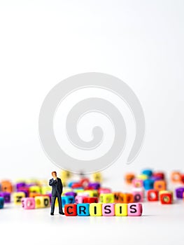 Miniature figure businessman in dark blue suit standing backside of colorful of CRISIS alphabet and thinking of the crisis will