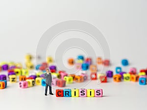 Miniature figure businessman in dark blue suit standing backside of colorful of CRISIS alphabet and thinking of the crisis will co