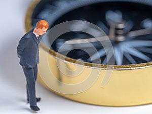 miniature figure businessman in dark blue suit standing on the side of golden compass. Concept for finding the way how to success