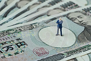 miniature figure businessman president or prime minister thinking standing on pile of japanese yen banknotes as financial