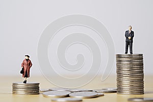 Miniature figure of businessman standing on higher than coins stacking of  businesswoman for inequality of gender male and female