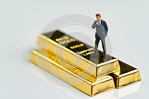 Miniature figure businessman standing and thinking on shiny gold