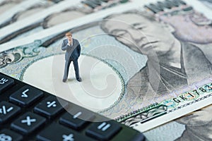 miniature figure businessman thinking standing on pile of japanese yen banknotes and calculator as financial safe haven or tax co