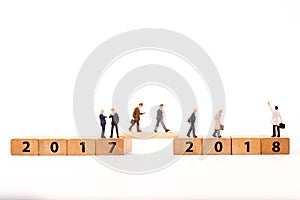 Miniature figure businessman walking on number wooden block across from 2017 to 2018