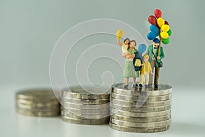 Miniature figure family holding balloon standing on stack of coins as financial business or happy concept