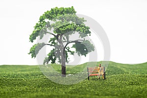 Miniature figure if an old man sitting on a bench under a tree