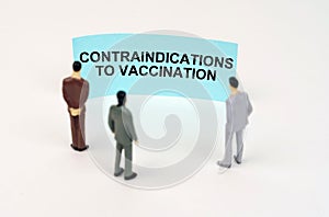 Miniature figures of people stand in front of a blue sign with the inscription - contraindications to vaccination photo
