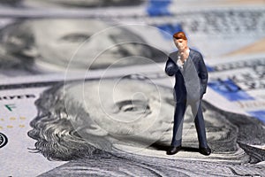 Miniature figurine businessman with 100 dollars banknote on background