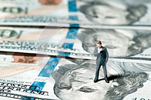 Miniature figurine businessman with 100 dollars banknote on background