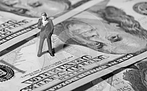 Miniature figurine businessman with 100 dollars banknote on background