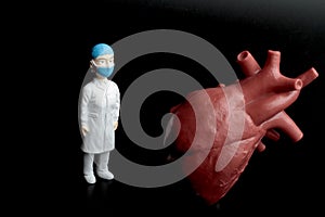 Miniature figurine of a cardiologist doctor with a giant heart on a black background photo