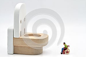 miniature figurine of a disabled man on a wheelchair looking at a huge wc