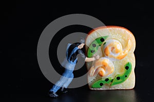 Miniature figurine of a man pushing a giant sandwich on a black background