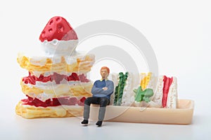 Miniature figurine of a man sitting on a giant sandwich and cake