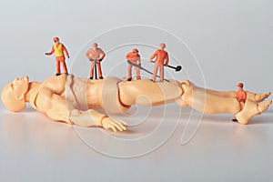 Miniature figurines of a team of men at work on a lying giant mannequin of a man