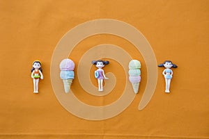 Miniature girl doll in swimming suit with icecreams on orange background