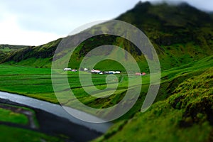 Miniature green farmland near mountain and river. On Iceland.