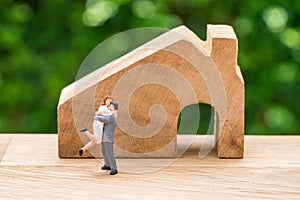 Miniature happy couple family standing with wooden house as prop