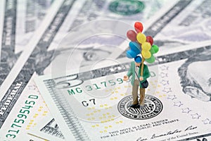 Miniature happy man holding colorful balloons on US Federal Reserve emblem on US dollars banknote as FED consider interest rate