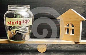 Miniature house and glass jar with coins on the scales. The inscription `mortgage`. credit for property / apartment. Business loan