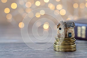 Miniature house and golden coins on wooden table and closed holy bible with bokeh background