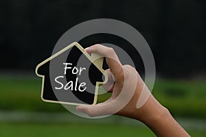 Miniature house in hands with text for sale on it.