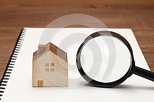 Miniature house, magnifying glass on blank notebook.