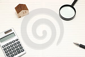 Miniature house, magnifying glass, calculator on blank notebook.